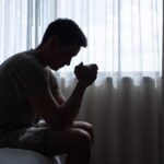 thoughtful man in a dark room with head down, Portrait of thoughtful sad man alone. prayer,  Fear, sadness, abuse, depression, addiction.