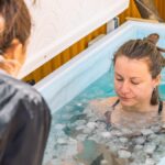 Girl or woman ice bathing in the cold water among ice cubes with the teacher or trainer. Wim Hof Method, cold therapy, breathing techniques, yoga and meditation