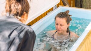 Girl or woman ice bathing in the cold water among ice cubes with the teacher or trainer. Wim Hof Method, cold therapy, breathing techniques, yoga and meditation