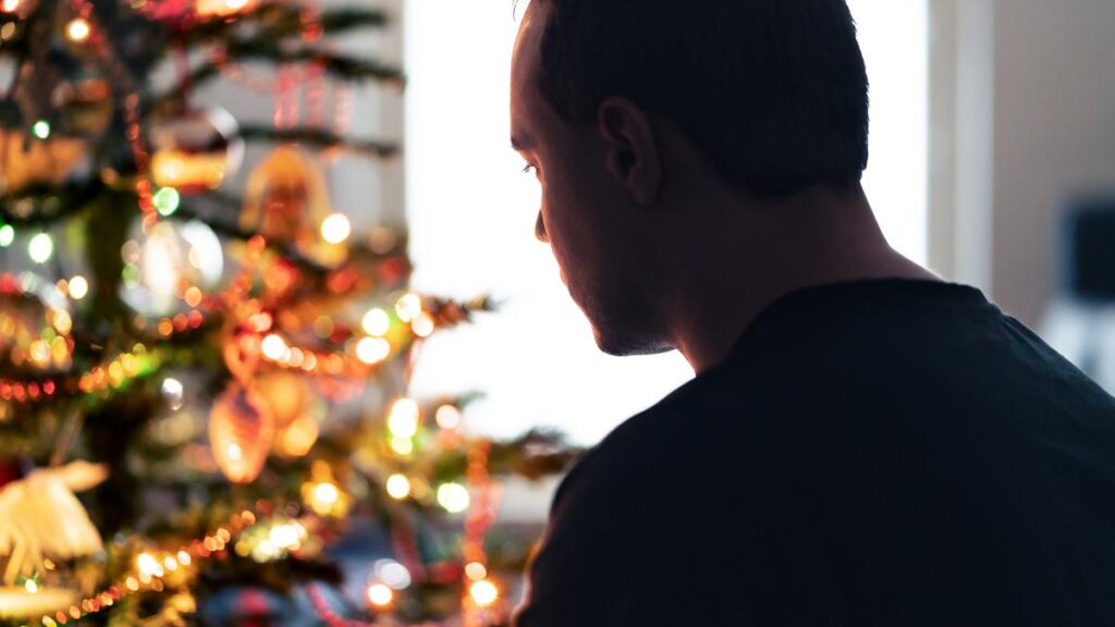 Lonely christmas with sad family conflict or grief on holiday. Man with stress, money problem or depression on Xmas. Unhappy tired person with loneliness in front of a decoration tree at winter home.