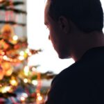 Lonely christmas with sad family conflict or grief on holiday. Man with stress, money problem or depression on Xmas. Unhappy tired person with loneliness in front of a decoration tree at winter home.